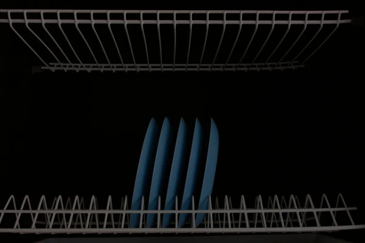 Five pale blue plates standing upright in a white wire dish rack against a black background.