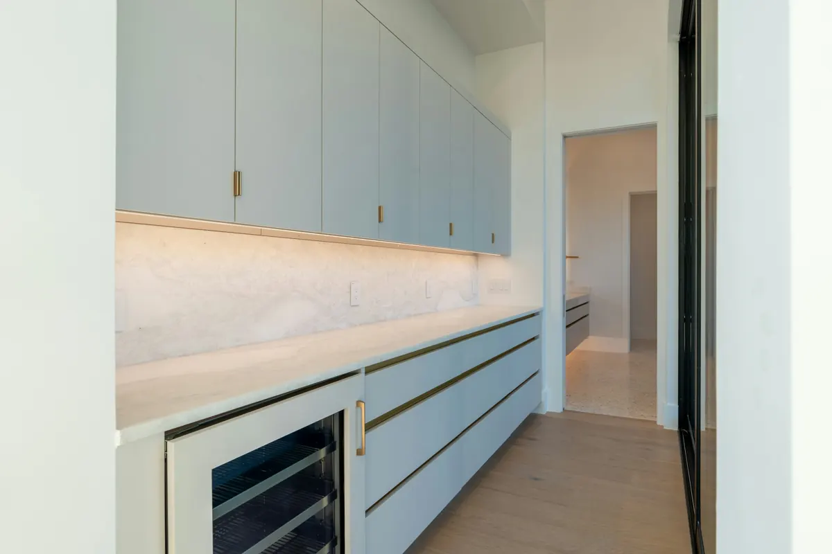 A butler's pantry with pale blue flat-front cabinets, a quartzite backsplash and an under-counter wine refrigerator with a glass door.